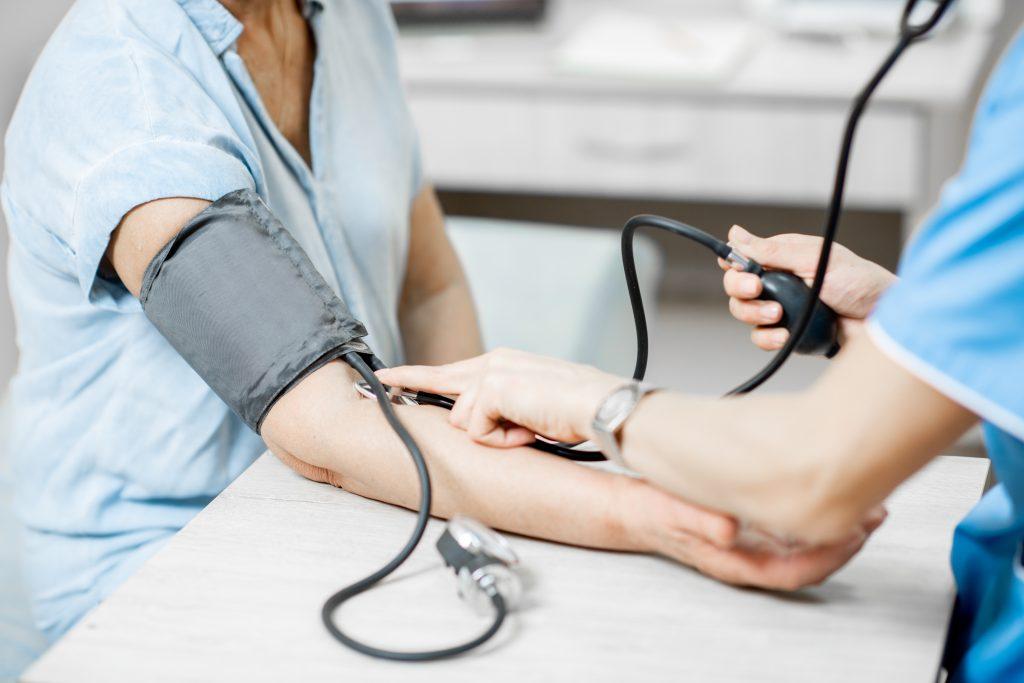 Cropped photo of a nurse measuring blood pressure of a senior woman patient during an examination in the clinic, close-up view with no face